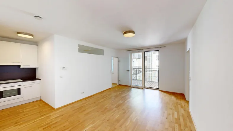 Heller offener Wohnbereich mit integrierter Küchenzeile, Parkettboden und Zugang zum Balkon.