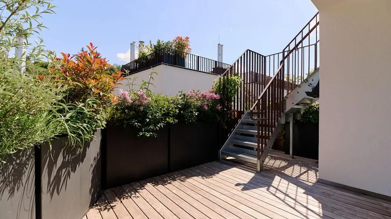 Geräumige Dachterrasse mit Holzbelag, Pflanzenkübeln und Zugang zu weiteren Ebenen.