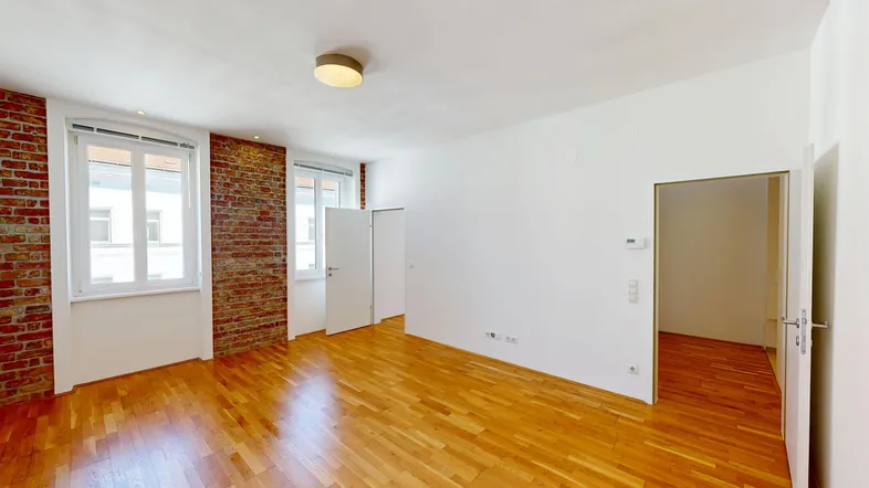 Heller Raum mit Holzboden, weißen Wänden und einer Akzentwand aus Ziegeln.