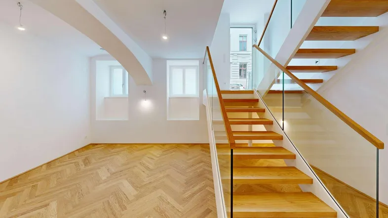 Heller, offener Wohnbereich mit moderner Holztreppe, Glasgeländer und Fischgrätparkettboden.