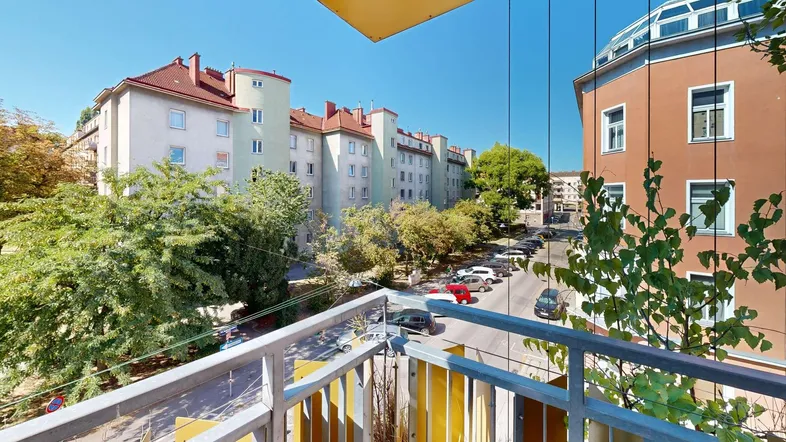 Blick vom Balkon auf die belebte Straße und die umliegenden Wohngebäude mit viel Grün.