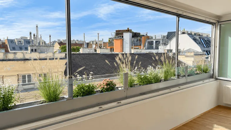 Heller, verglaster Balkon mit Pflanzen und weitem Blick über die Dächer der Stadt.
