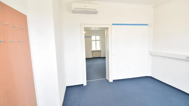 Leerer Raum mit blauer Auslegware, Klimaanlage und Zugang zu einem weiteren Zimmer.
