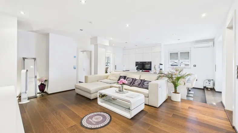 Helles, offenes Wohnzimmer mit modernem Sofa, Holzboden und integrierter Küche im Hintergrund.