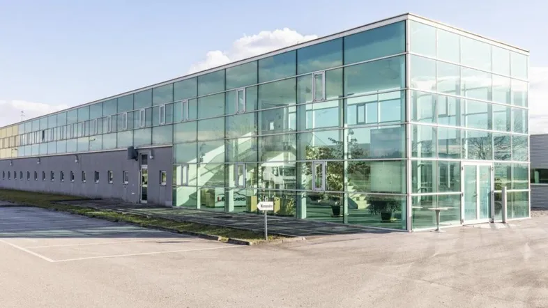 Modernes Geschäftsgebäude mit großer Glasfassade und umliegendem Parkplatz unter blauem Himmel.