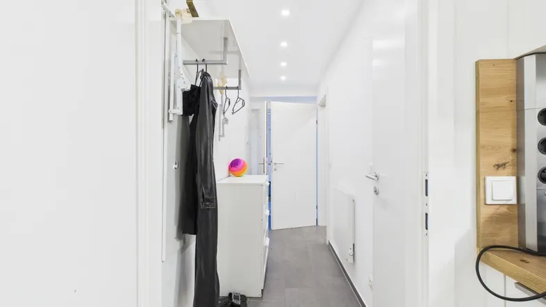 Langer, heller Flur mit Garderobe, Einbaustrahlern und modernen Fliesen.