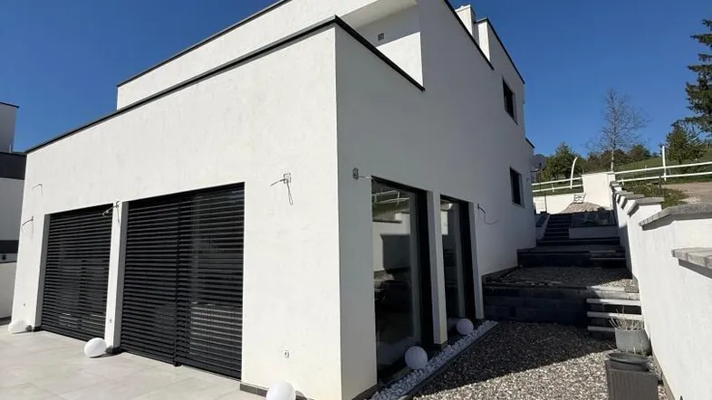 Seitliche Ansicht der modernen Villa mit Garagentoren und gepflastertem Zugangsbereich.