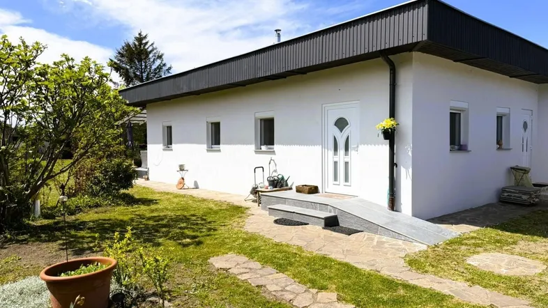 Weißes Einfamilienhaus mit dunklem Dachüberstand, gepflegtem Vorgarten und barrierefreiem Zugang.