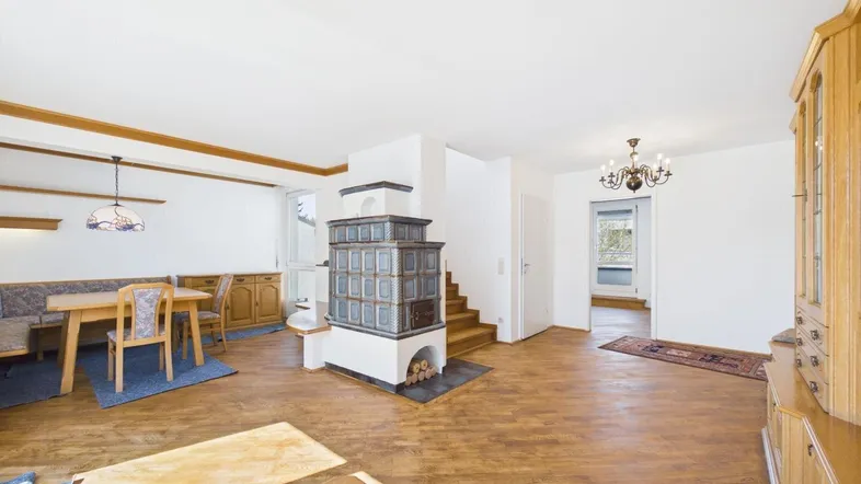Gemütlicher Wohn-Essbereich mit traditionellem Kachelofen, Holzboden und rustikalen Möbeln.