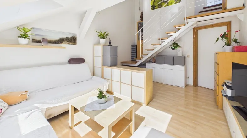 Helles Wohnzimmer mit Dachschrägen, Holzboden und offener Treppe zur oberen Ebene.