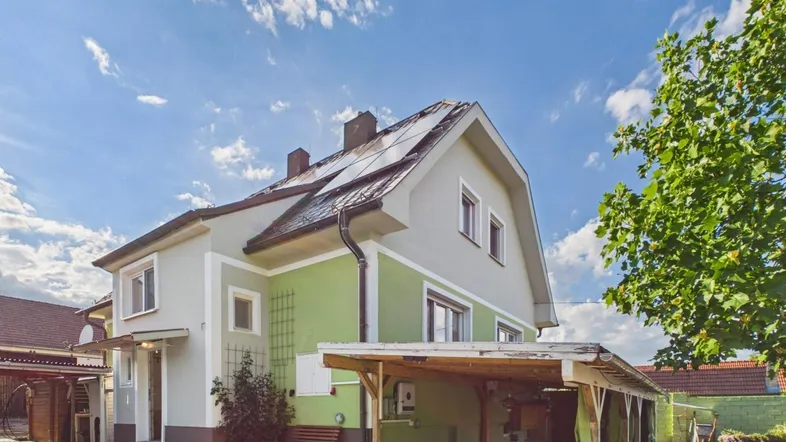 Seitliche Ansicht des Hauses mit Solarpaneelen auf dem Dach und einem überdachten Bereich.