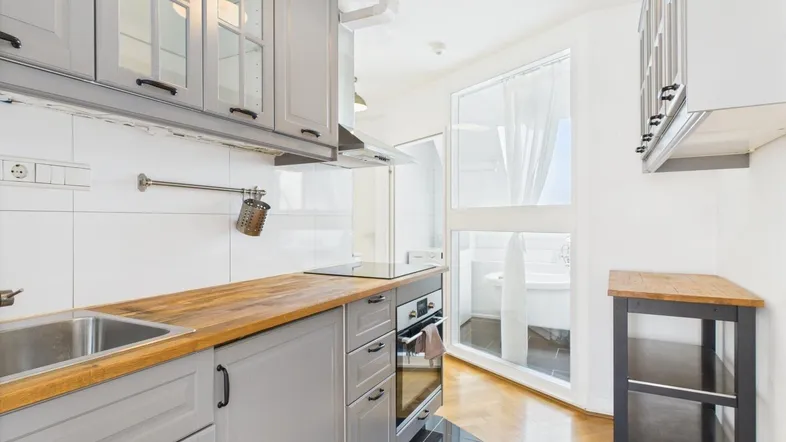 Moderne Küche mit grauen Schränken, Holzarbeitsplatte und Blick auf einen Balkon.