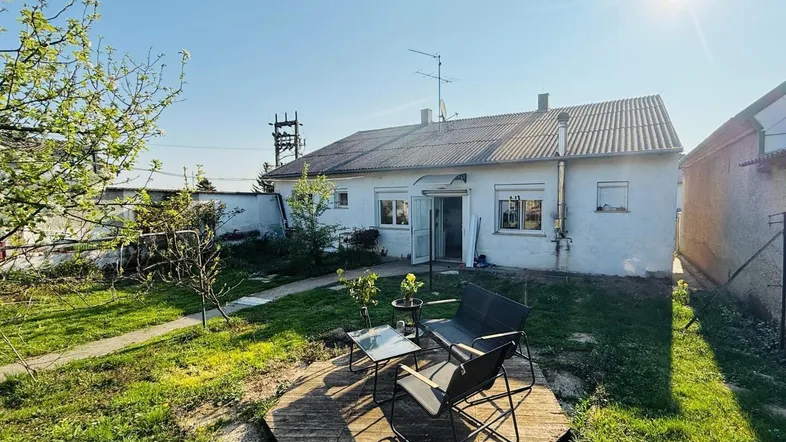 Kleiner Gartenbereich hinter dem Haus mit Sitzgelegenheit und viel Grünfläche unter strahlendem Himmel.
