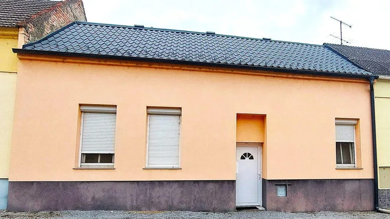 Einfaches Einfamilienhaus mit pastellfarbener Fassade und Rollläden an den Fenstern.