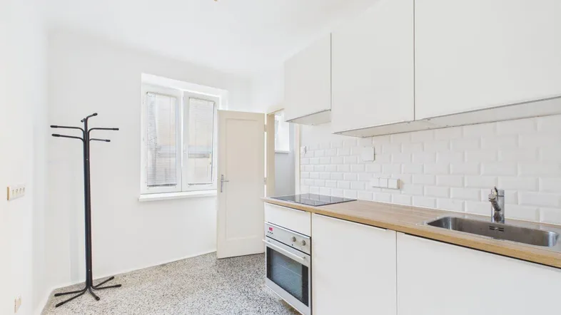 Helle Küche mit weißen Schränken, Holztheke, modernen Geräten und Terrazzoboden.