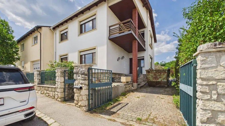 Mehrstöckiges Wohnhaus mit Balkonen, gepflasterter Einfahrt und Steinmauer.