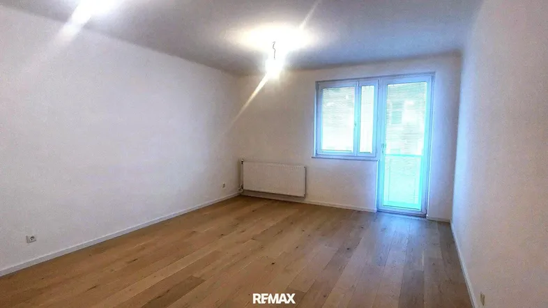 Helles Zimmer mit Holzboden, weißen Wänden und großem Fenster, ideal als Wohn- oder Schlafzimmer.