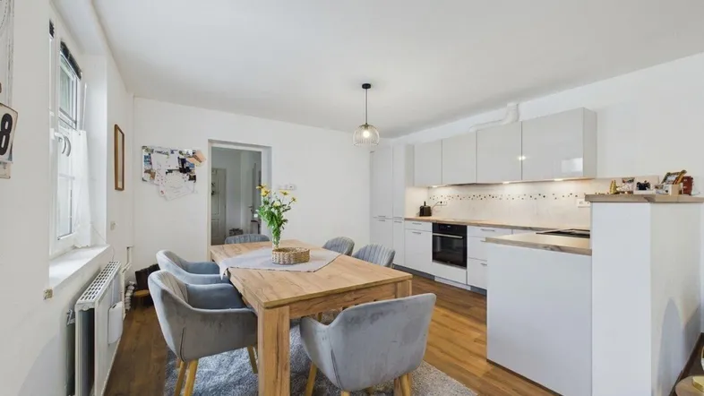 Moderne Küche mit Essbereich, weißen Hochglanzschränken, Holztisch und Laminatboden.
