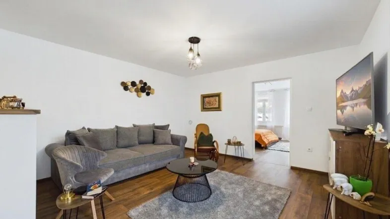 Helles Wohnzimmer mit bequemer Couch, Teppich und Holzboden, mit Blick in ein weiteres Zimmer.