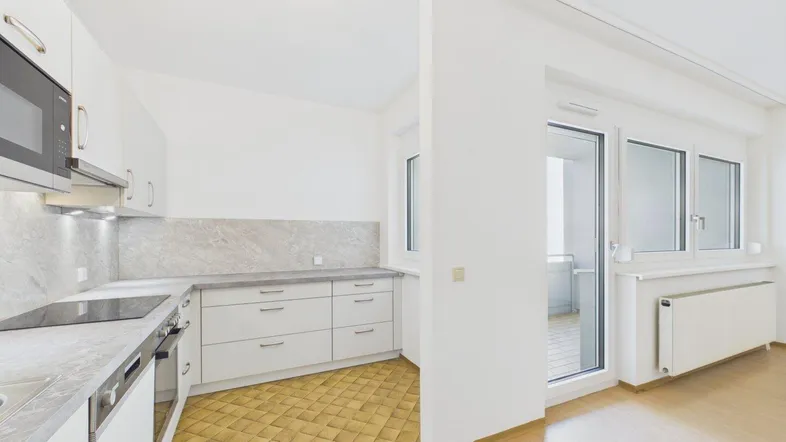 Helle Küche mit weißen Schränken, Fliesenboden und direktem Zugang zum Balkon.