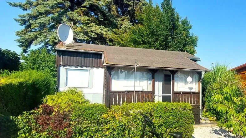 Kleines Haus mit Satellitenschüssel und gepflegter Hecke im Grünen unter blauem Himmel.