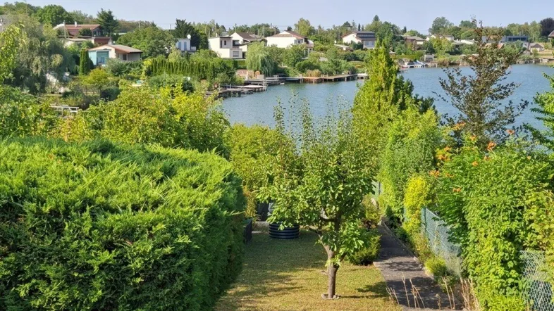 Gepflegter Gartenbereich mit üppigem Grün und direktem Blick auf den See unter blauem Himmel.