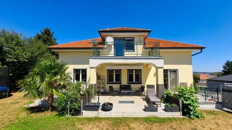 Geräumige Terrasse mit Gartenmöbeln und Zugang zum Garten, ergänzt durch einen Balkon im Obergeschoss.
