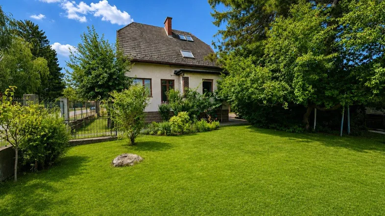 Freistehendes Einfamilienhaus mit großem, gepflegtem Rasen und umgebenden Bäumen unter blauem Himmel.