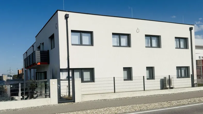 Modernes, weißes Gebäude mit dunklen Fenstern und einem kleinen Balkon an der Seite.