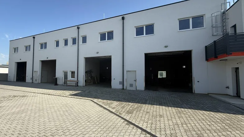 Moderne Gewerbeimmobilie mit mehreren Garagentoren und gepflastertem Vorplatz unter blauem Himmel.