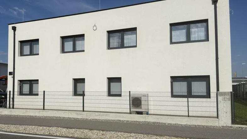 Moderne weiße Fassade eines Geschäftsgebäudes mit dunklen Fenstern und einem Zaun davor.