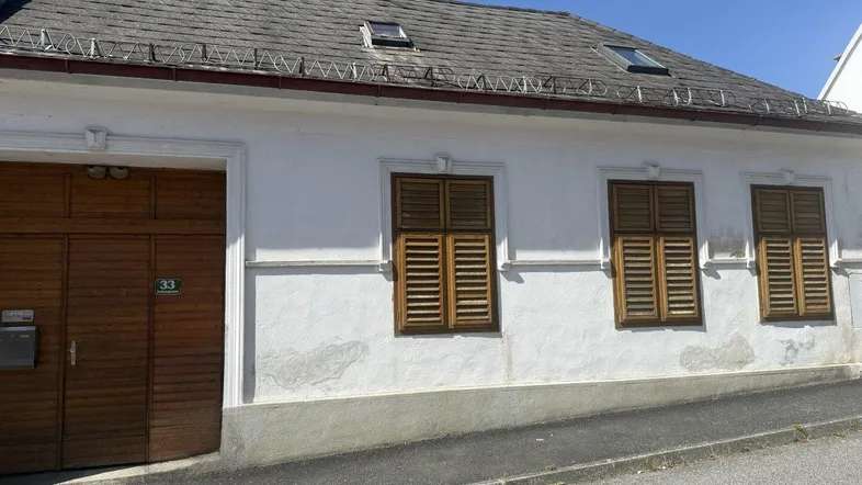 Weißes Haus mit Holztoren und Fensterläden, typisch für ländliche Architektur.
