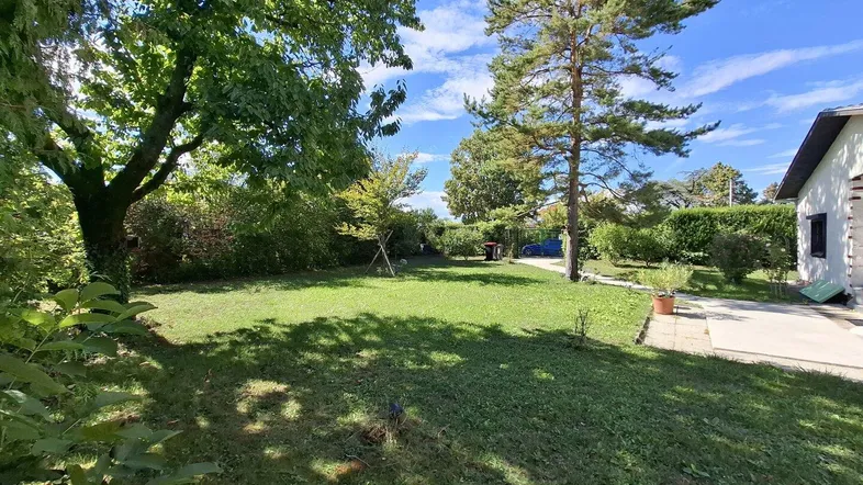 Großer, gepflegter Garten mit Rasenfläche und altem Baumbestand unter blauem Himmel.