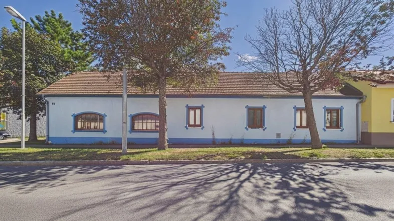 Einfaches Haus mit weiß-blauer Fassade und braunem Ziegeldach an einer Straße.