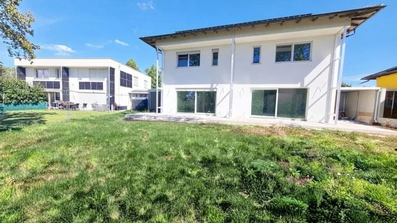 Modernes weißes Haus mit großem Garten und viel Grünfläche unter blauem Himmel.