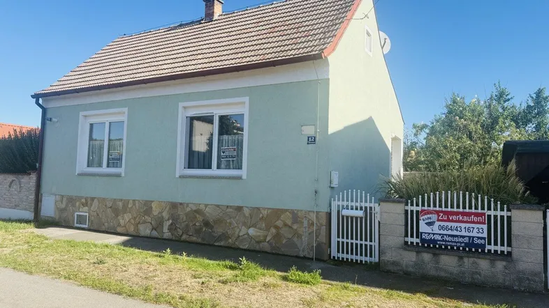 Charmantes Einfamilienhaus mit hellgrüner Fassade und Steinsockel in sonniger Lage.