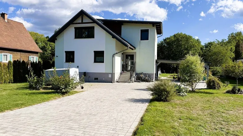 Vorderansicht eines Einfamilienhauses mit gepflasterter Auffahrt und grünem Vorgarten unter blauem Himmel.