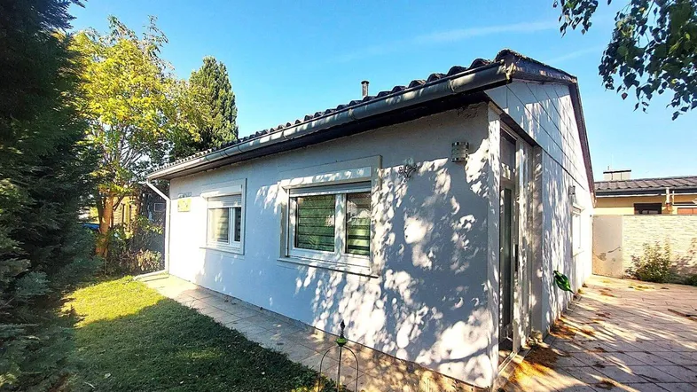 Kleines Einfamilienhaus mit weißer Fassade, Gartenbereich und blauer Himmel an einem sonnigen Tag.