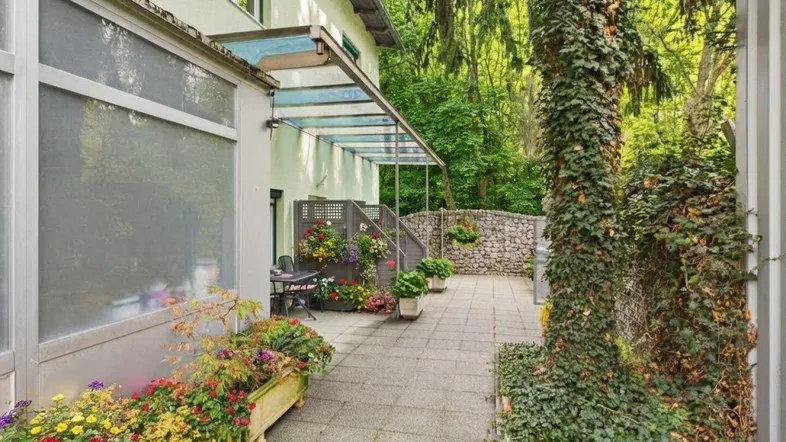 Gepflasterte Terrasse mit Blumenkästen und Sitzgelegenheiten, umgeben von üppigem Grün.