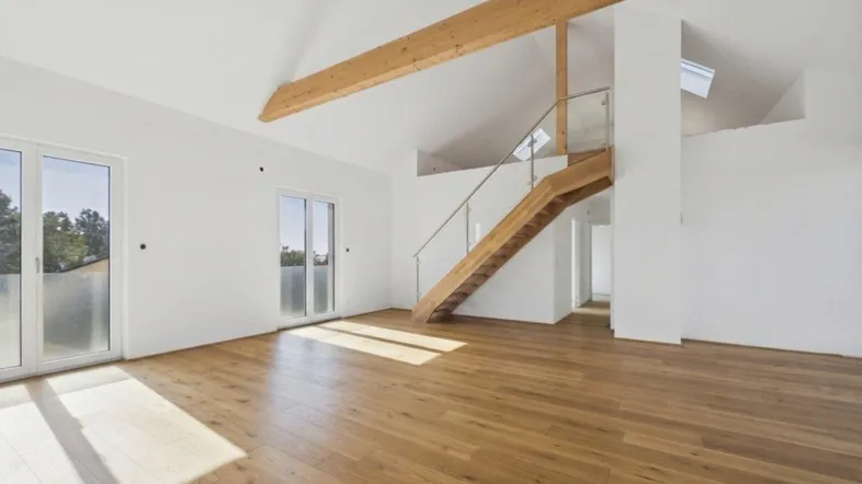 Helles, offenes Wohnzimmer mit Holzboden, hohen Decken, sichtbaren Holzbalken und Zugang zu einem Balkon.