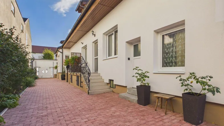 Außenansicht des Hauses mit gepflasterter Auffahrt und bepflanzten Bereichen unter blauem Himmel.