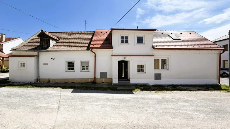 Ansicht des weißen Hauses mit rotem Ziegeldach und mehreren Fenstern unter blauem Himmel.