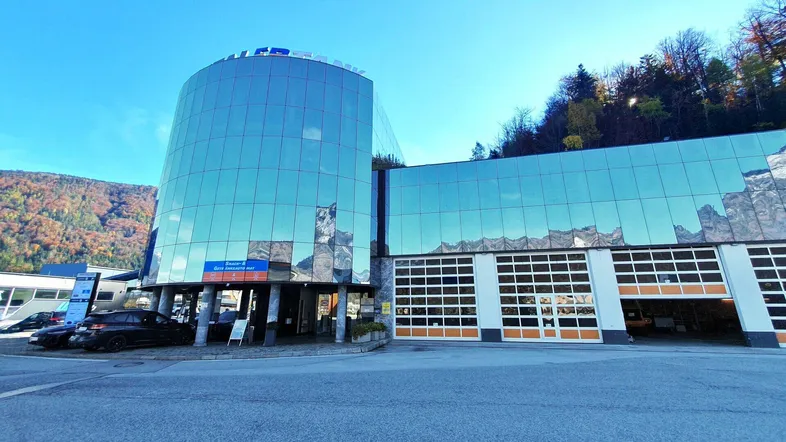 Modernes Geschäftsgebäude mit Glasfassade und Garagentoren, umgeben von Bergen und Parkplätzen.
