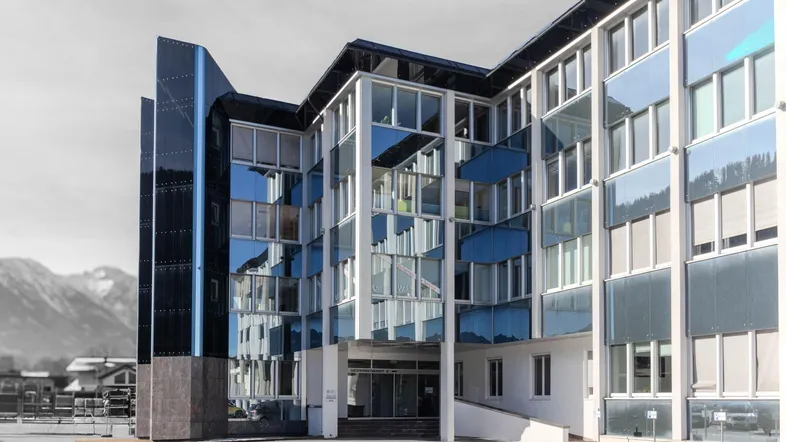 Modernes Geschäftsgebäude mit Glasfassade und reflektierenden Fenstern vor einer Bergkulisse.