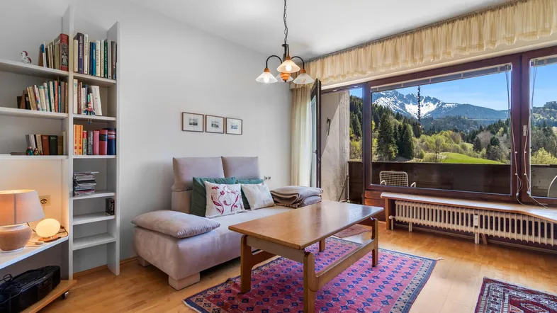 Helles Wohnzimmer mit Holzboden, gemütlichem Sofa und großem Fenster mit Bergblick.