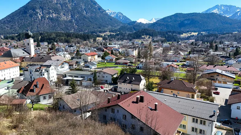 Panoramablick auf eine malerische Stadt mit traditionellen Häusern und majestätischen Bergen im Hintergrund.