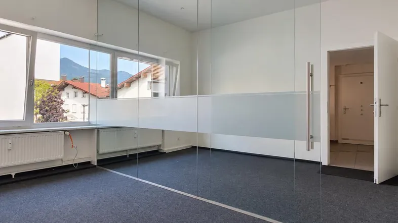 Heller Büroraum mit Teppichboden, Glasabtrennung und Bergblick durch große Fenster.