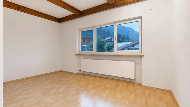 Helles Zimmer mit Holzbalkendecke, Parkettboden und Blick auf die umliegenden Berge.