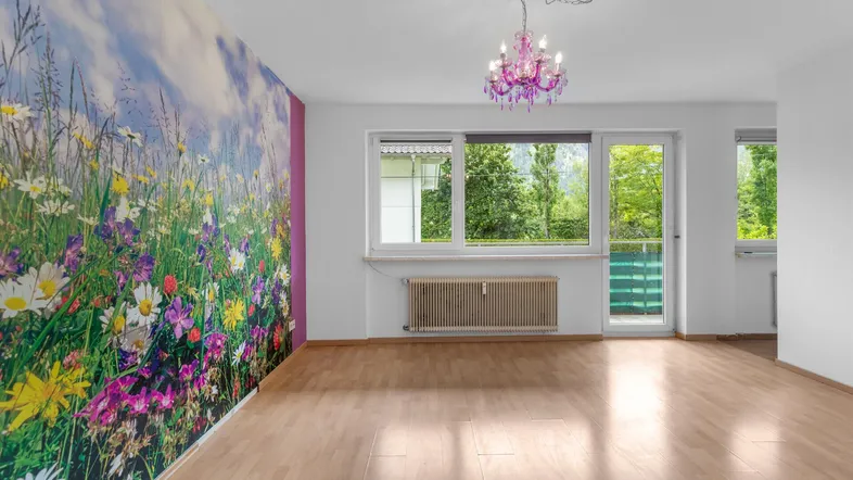 Helles Zimmer mit auffälliger Blumenwandtapete, Holzboden und Blick ins Grüne.