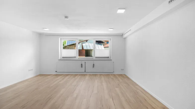 Helles, leeres Zimmer mit modernem Laminatboden und einem Fenster mit Blick nach draußen.